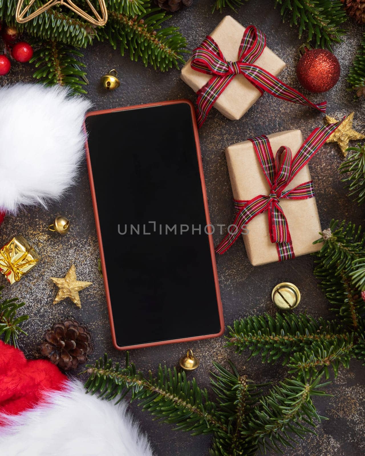 Mobile phone between Christmas decorations, wrapped gift boxes and green fir branches top view. Cell phone mockup with copy space. Christmas or New Year Holiday atmospheric flat lay