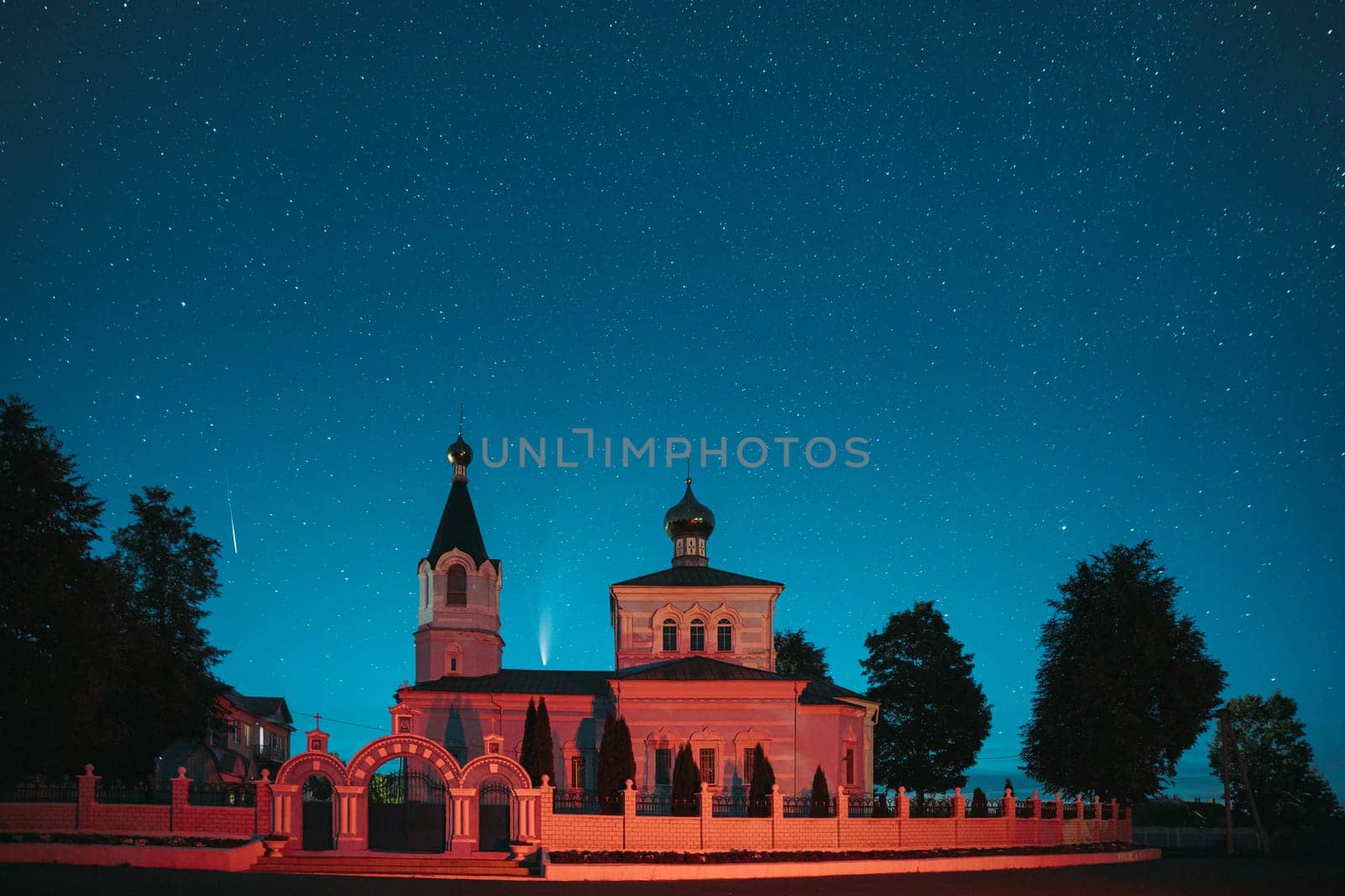 Korma Village, Dobrush District, Belarus. Comet Neowise C2020F3 And Meteor In Night Starry Sky Above St. John The Korma Convent Church In Korma Village. Famous Orthodox Church And Historic Heritage.