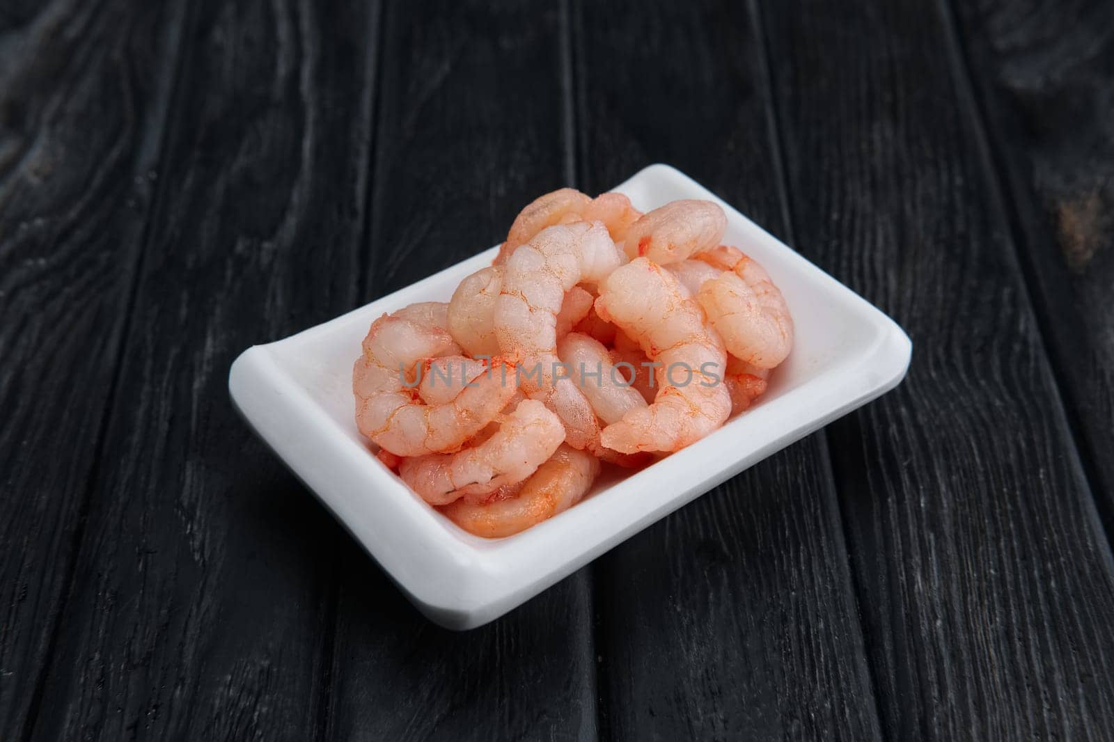 Small boiled peeled shrimps in small plate on dark wooden background