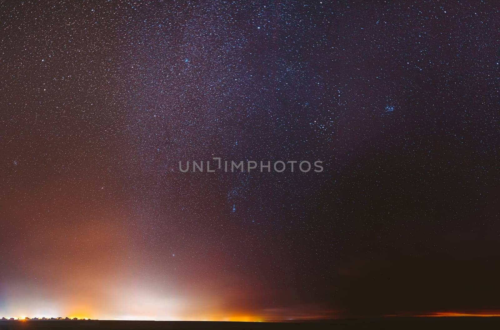 Night Starry Sky With Glowing Stars Above Dark Dround. Bright Glow Of Stars. Illumination Lights Of Small Town Or Village. Milky Way Galaxy.