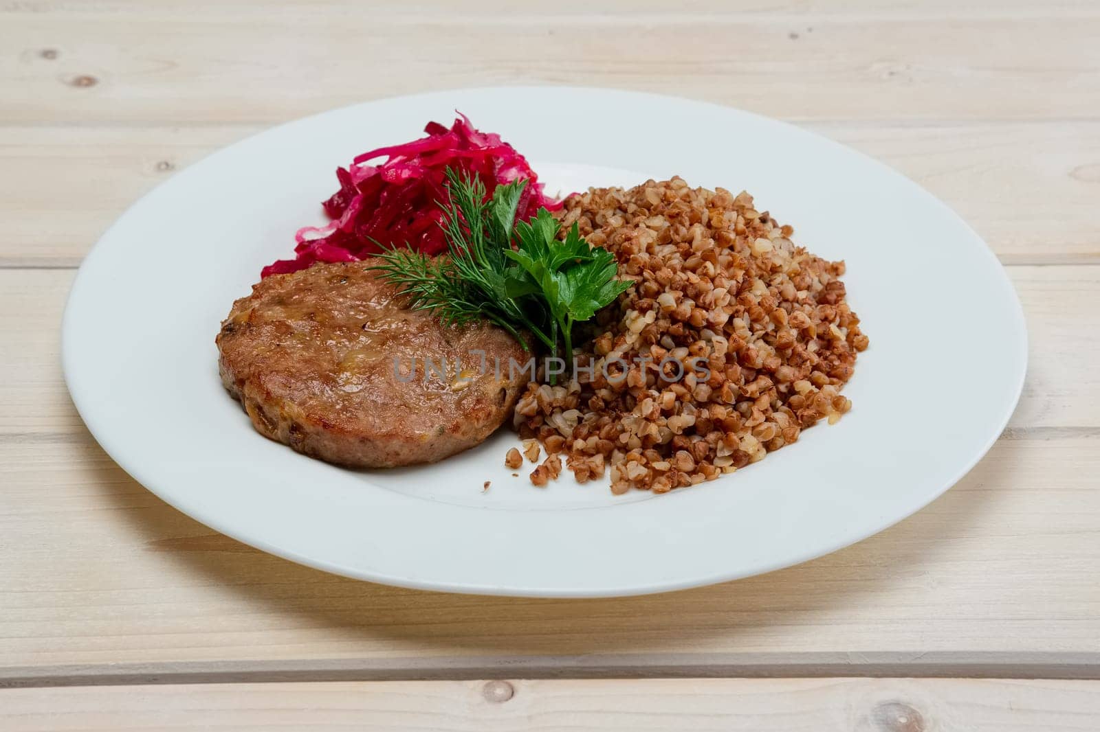 Portion of fried beef cutlet, boiled buckwheat and pickled red cabbage