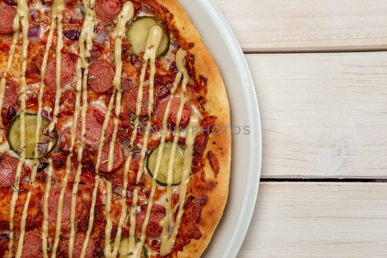 Top view of pizza with thin sausage and pickled cucumber