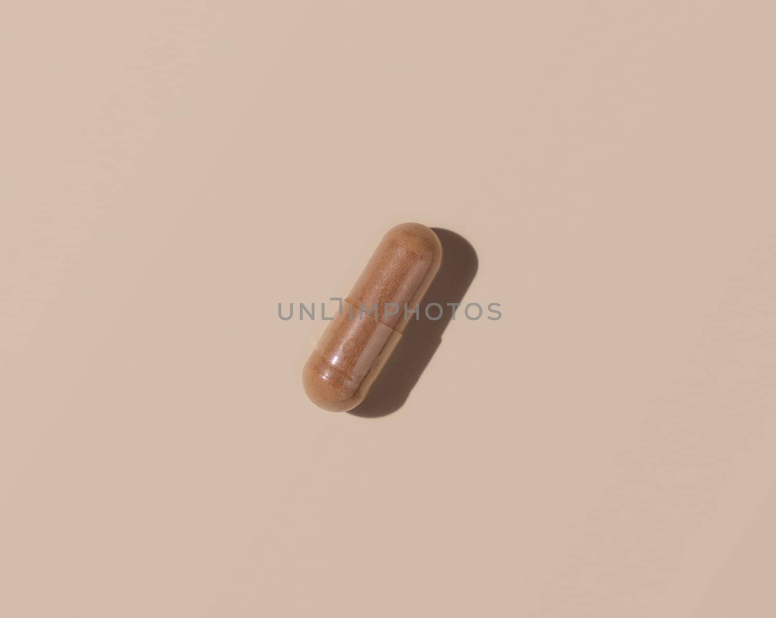 Brown medical capsule on light beige top view, hard shadows. Preventive medicine and healthcare, taking dietary supplements and vitamins. Minimal composition