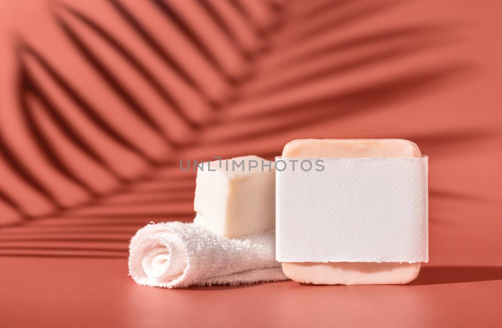 Handmade soap bars with blank label and small face towel on pink close up, palm leaf hard shadows. Skincare beauty product package. Exotic natural cosmetics, pastel minimal composition..