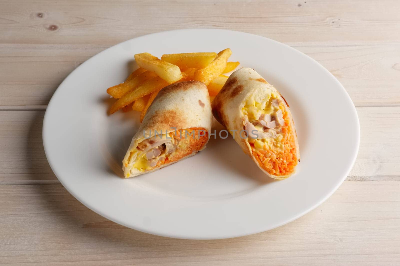 Meat, spicy carrot, cabbage and cheese rolled up in thin pitta bread on a plate