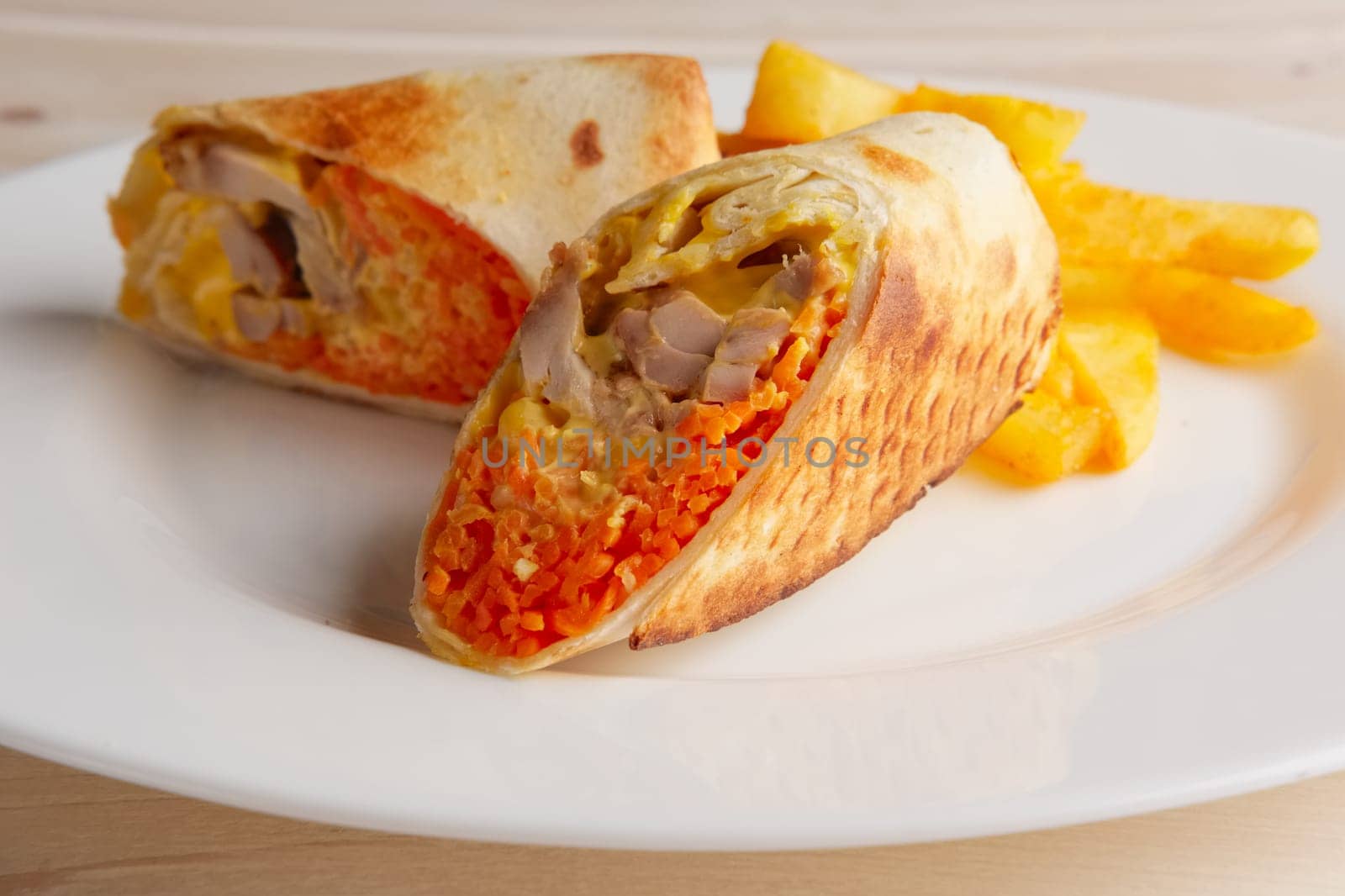 Meat, spicy carrot, cabbage and cheese rolled up in thin pitta bread on a plate