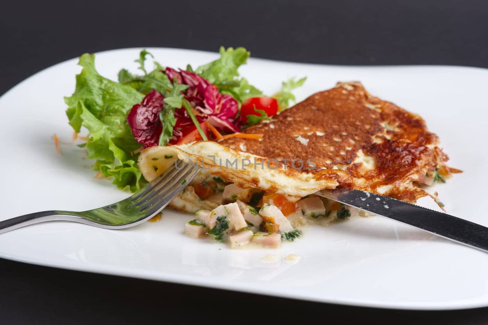Cutting with knife omelet with ham and vegetables
