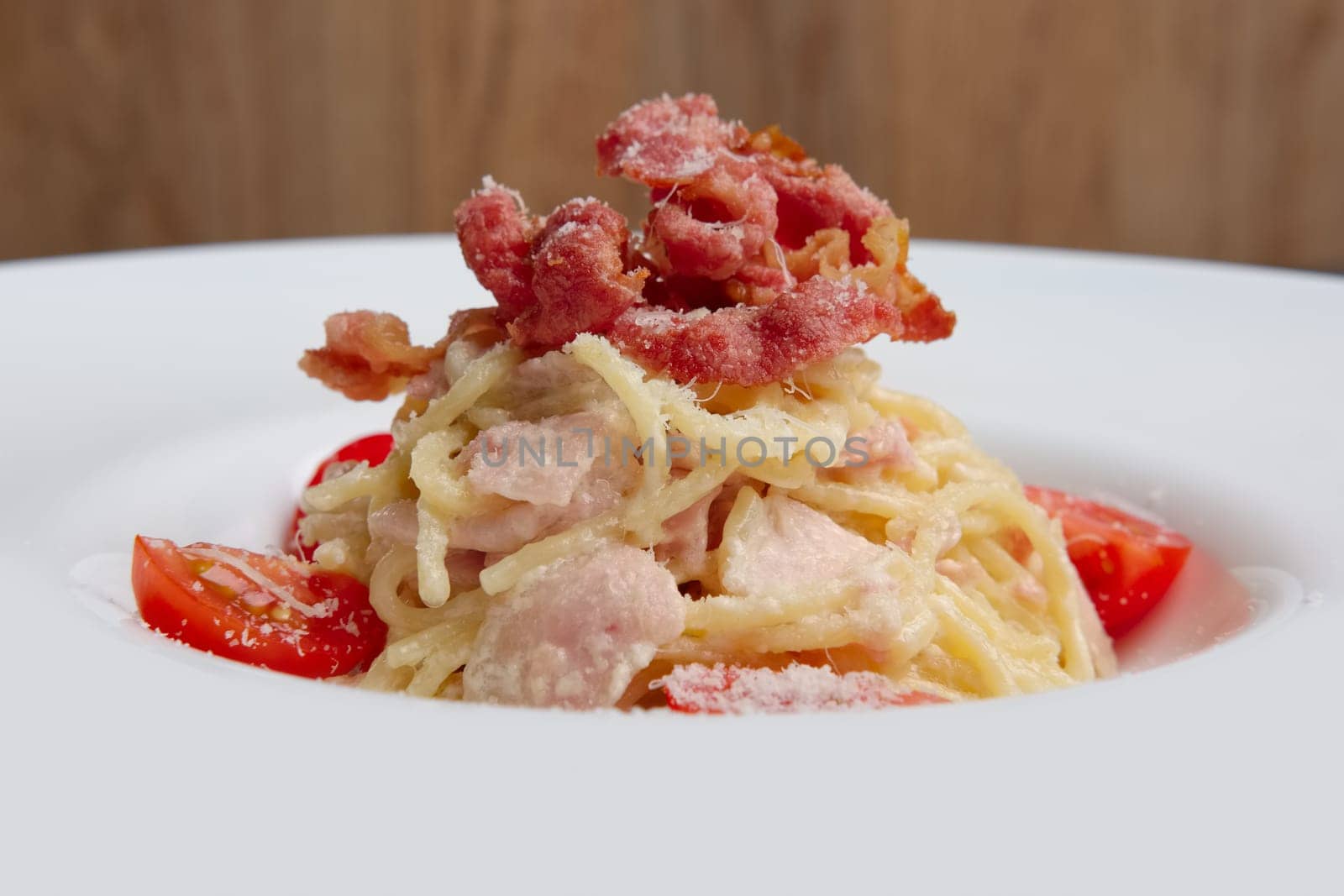 Plate with pasta served with bacon and ham, decorated with tomato cherry, closeup