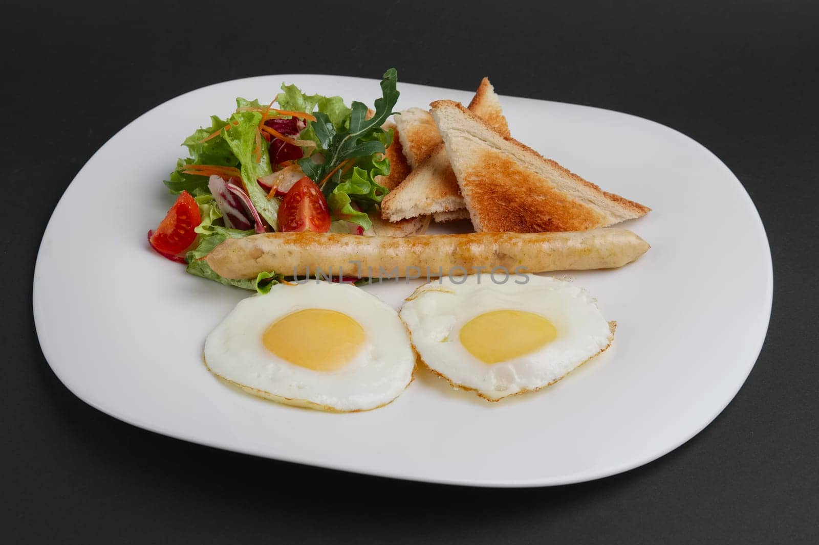 Fried eggs with homemade sausage, toasts and fresh tomato and salad on a plate
