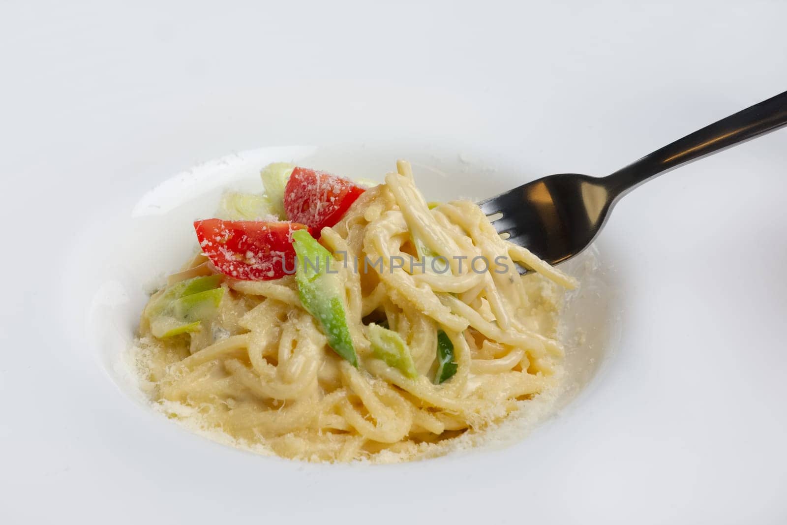 Fork in plate with pasta served with bacon and ham, decorated with tomato cherry