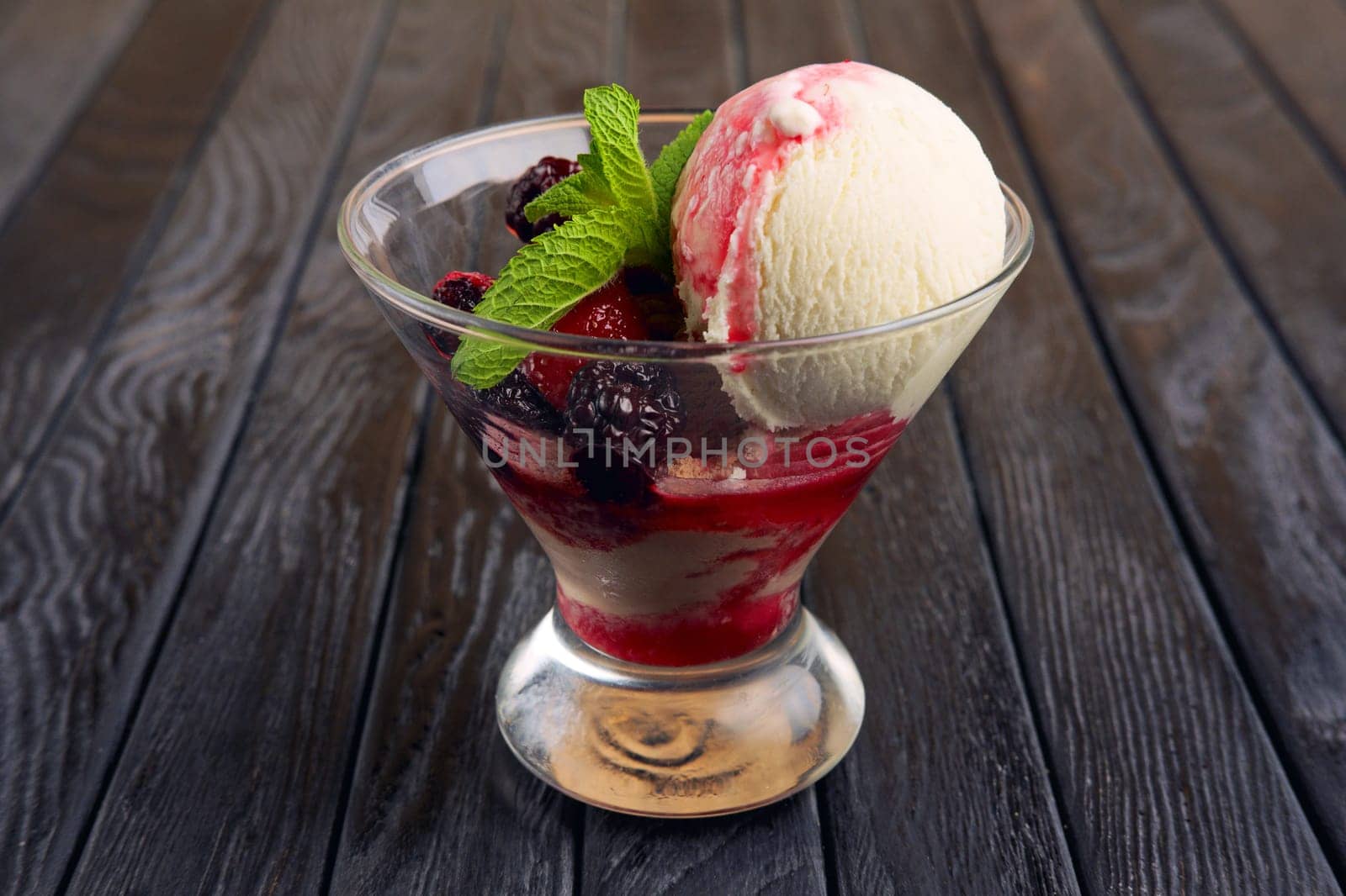 A cup of raspberries ice cream decorated with dewberry and mint leaves