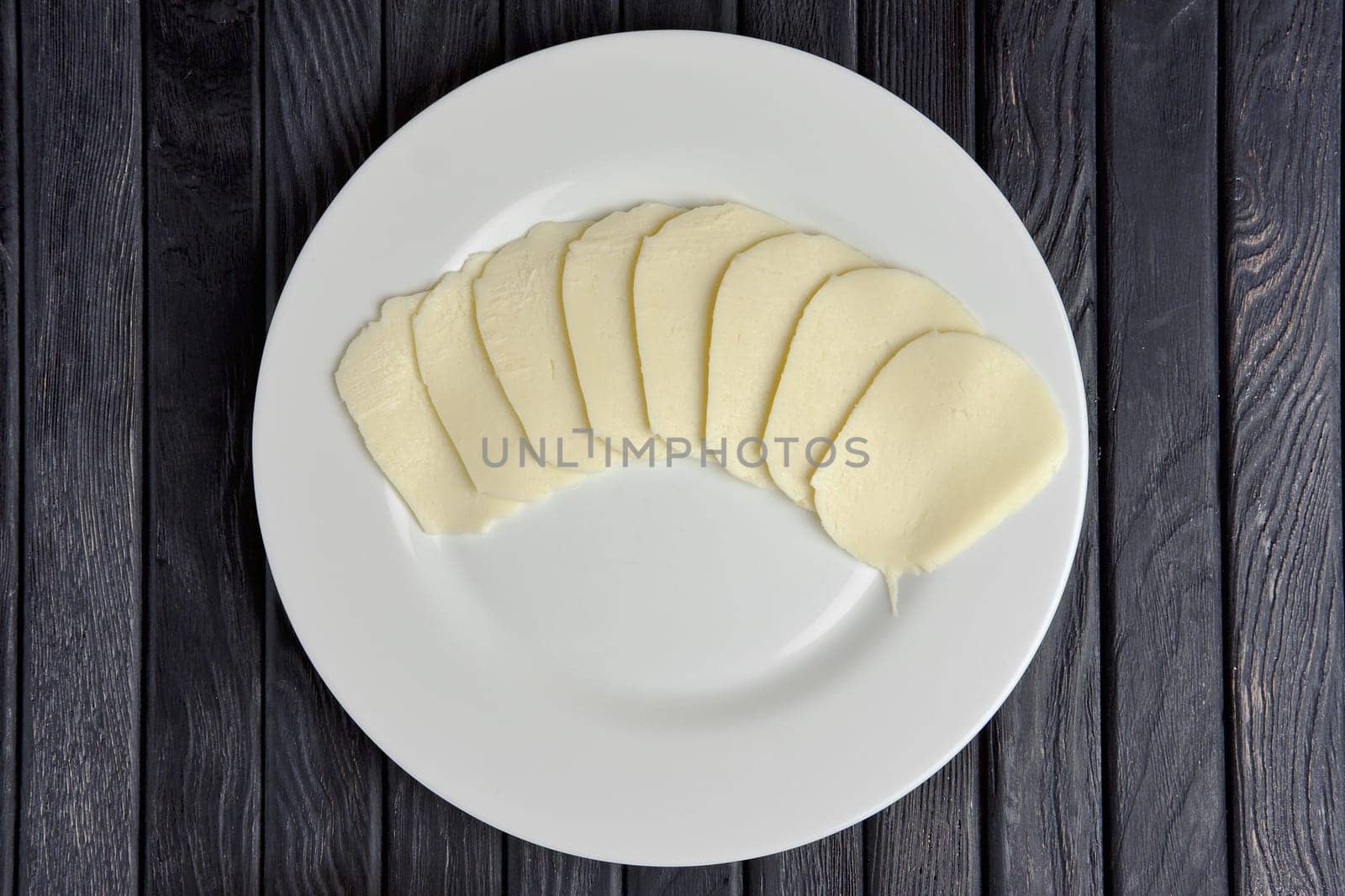 Top view of mozzarella  cheese slices on round plate on wooden table.