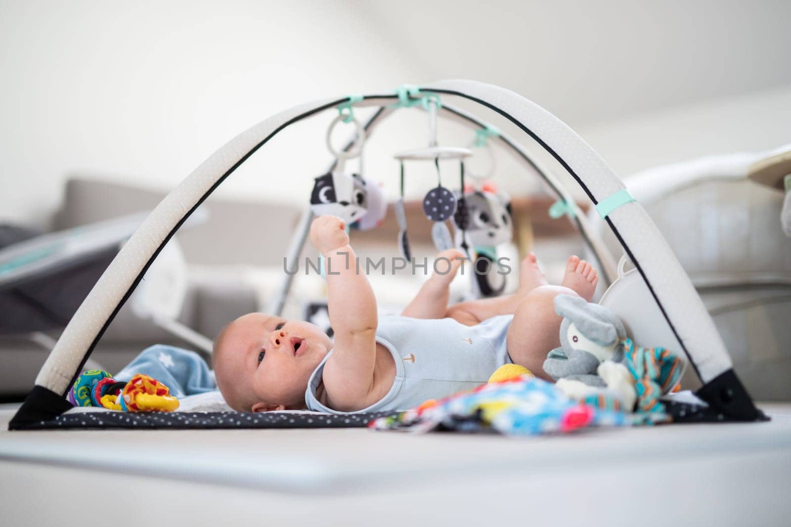 Cute baby boy playing with hanging toys arch on mat at home Baby activity and play center for early infant development. Baby playing at home.