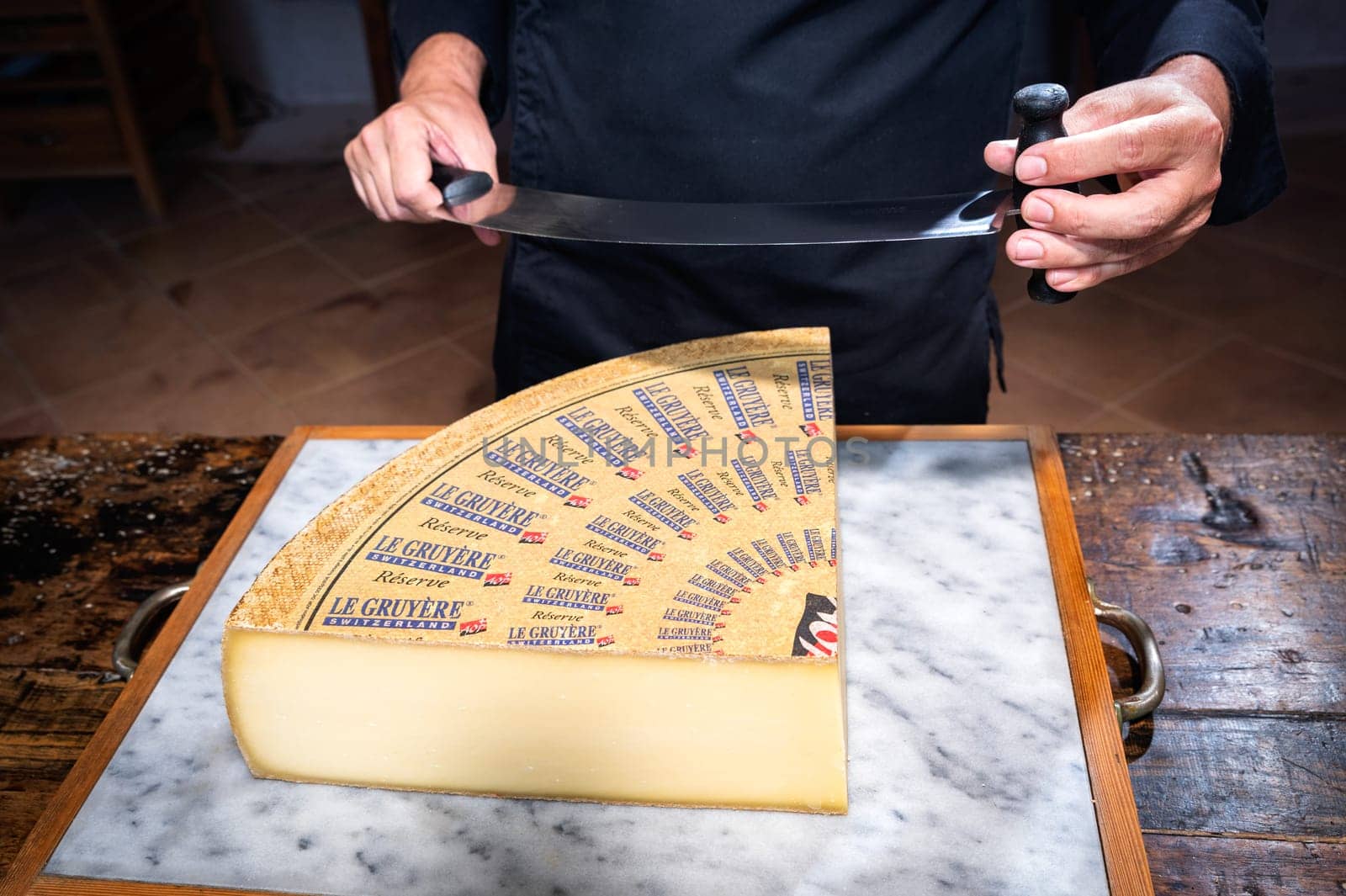 July 11 2022, Lyon, France : A man cuts a portion of The Gruyère with a wire, the famous swiss cheese in a cellar on a marbble background