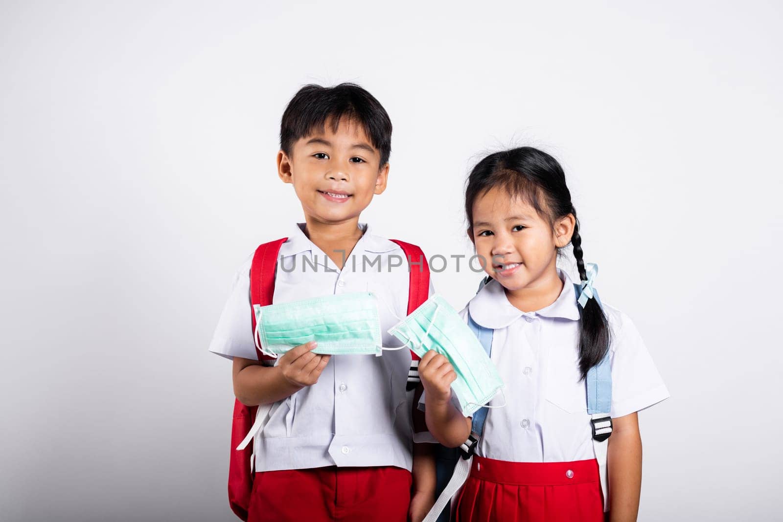 Two Asian student kid girl boy brother sister wearing student thai uniform holding protect mask ready to go to school in studio shot isolated on white background, new normal back to school