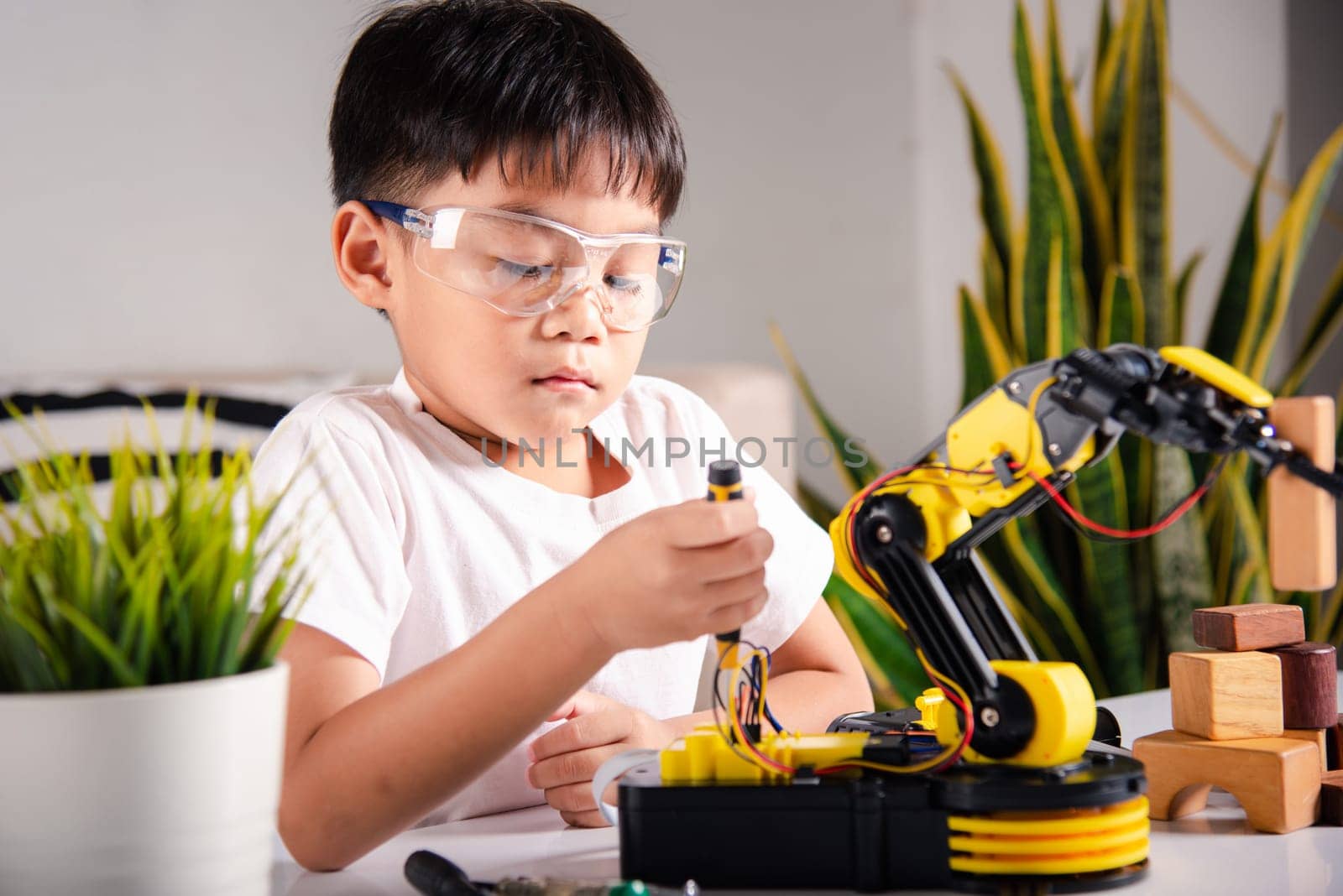 Happy Asian little kid boy using screwdriver to fixes screws robotic machine arm in home workshop, child learning repairing get lesson control robot arm, Technology future science education concept