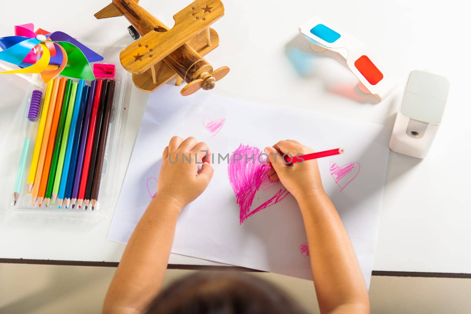 Happy child little girl colorful drawing pink heart on white paper, Asian cute kid preschooler smiling draw color love picture card at home, Valentine's or Mother's Day or Father's Day