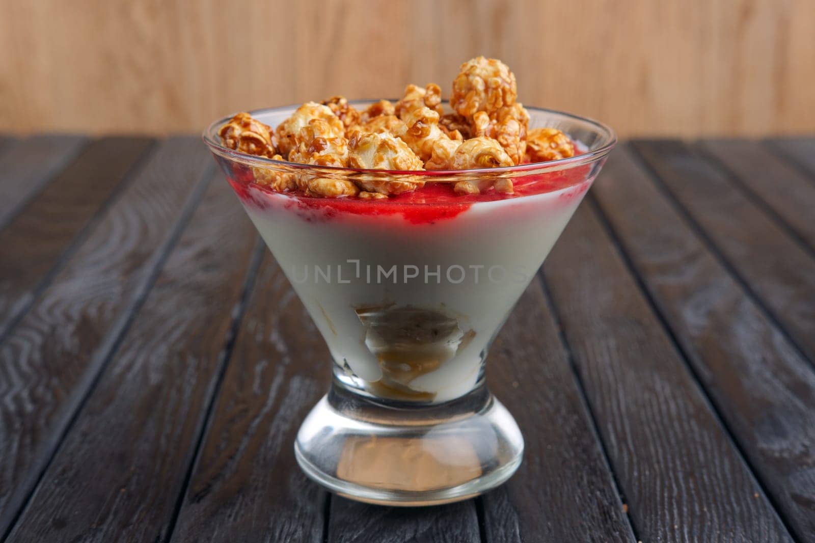 A cup of yoghurt with cherry syrup decorated with caramel popcorn