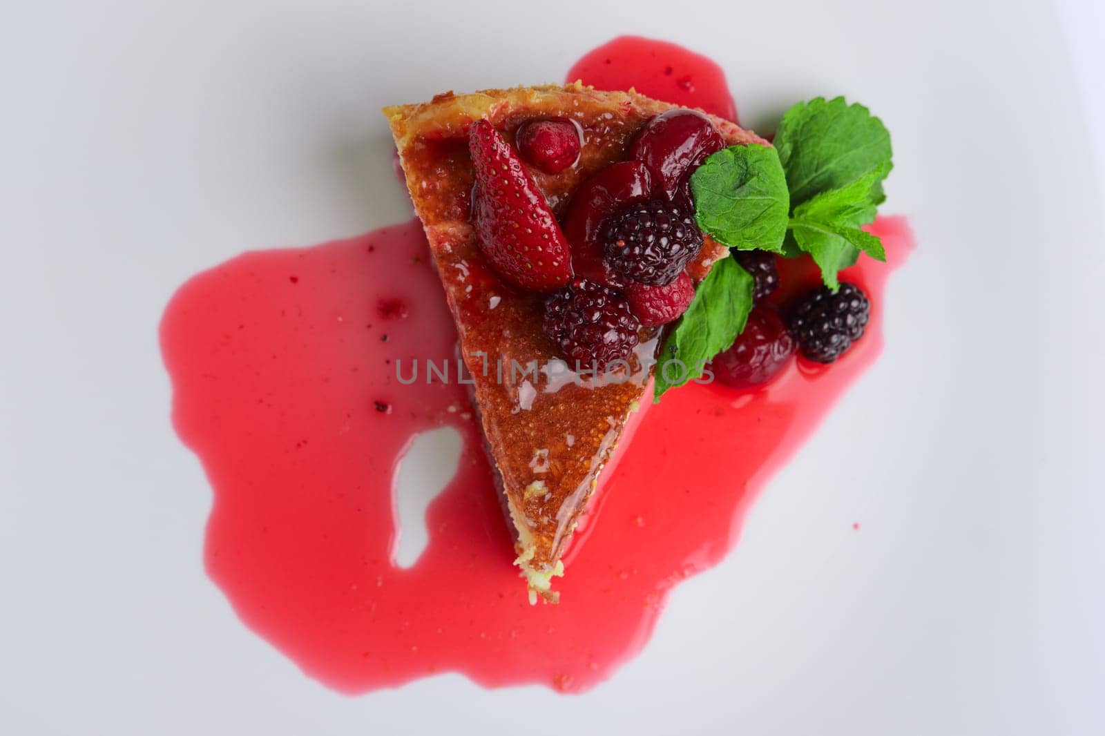 Top view of cheesecake with cherry, strawberry and dewberry decorated with syrup and mint leaves