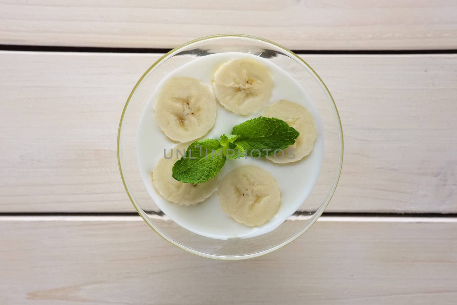 Top view of glass with yogurt and raw honey topped with sliced bananas and mint leaf. Selective focus photo.