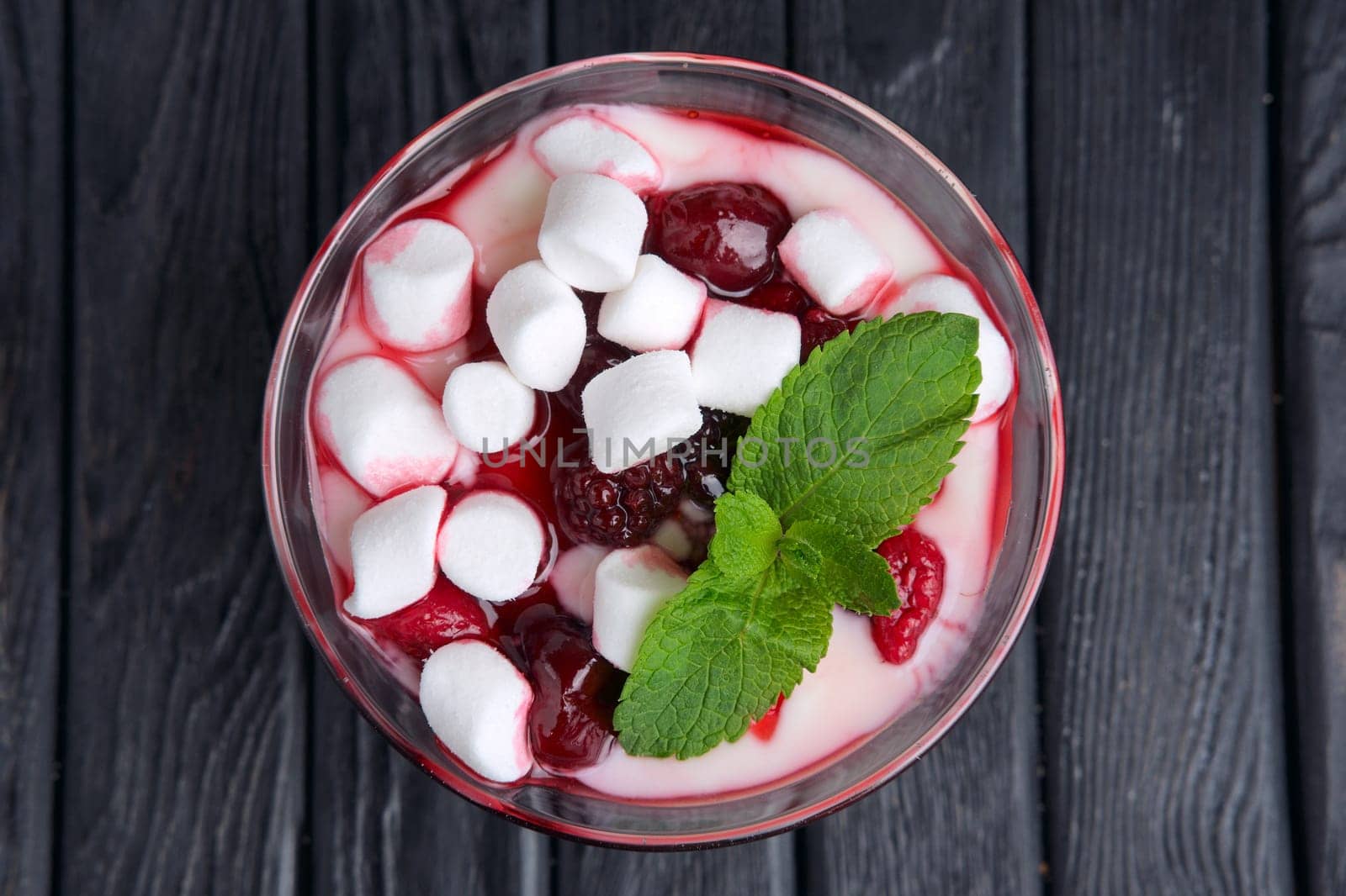 A glass of youghurt with marshmallow and raspberries decorated with mint leaves. Top view.