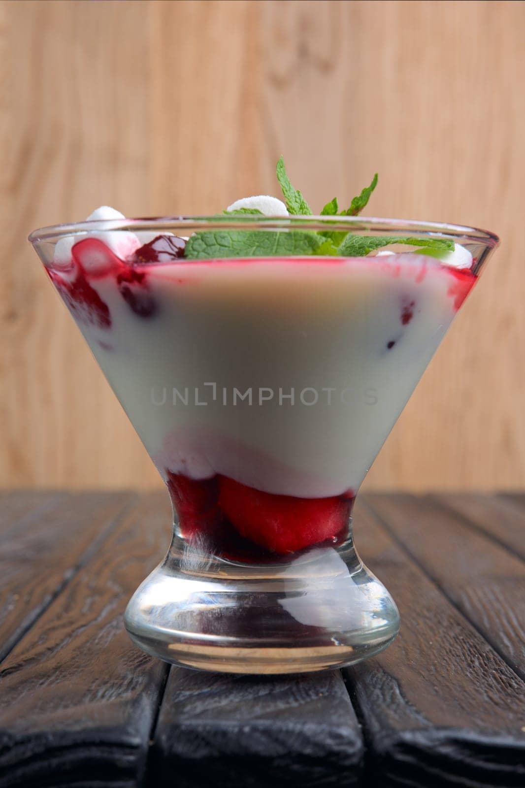 A glass of youghurt with marshmallow and raspberries decorated with mint leaves.