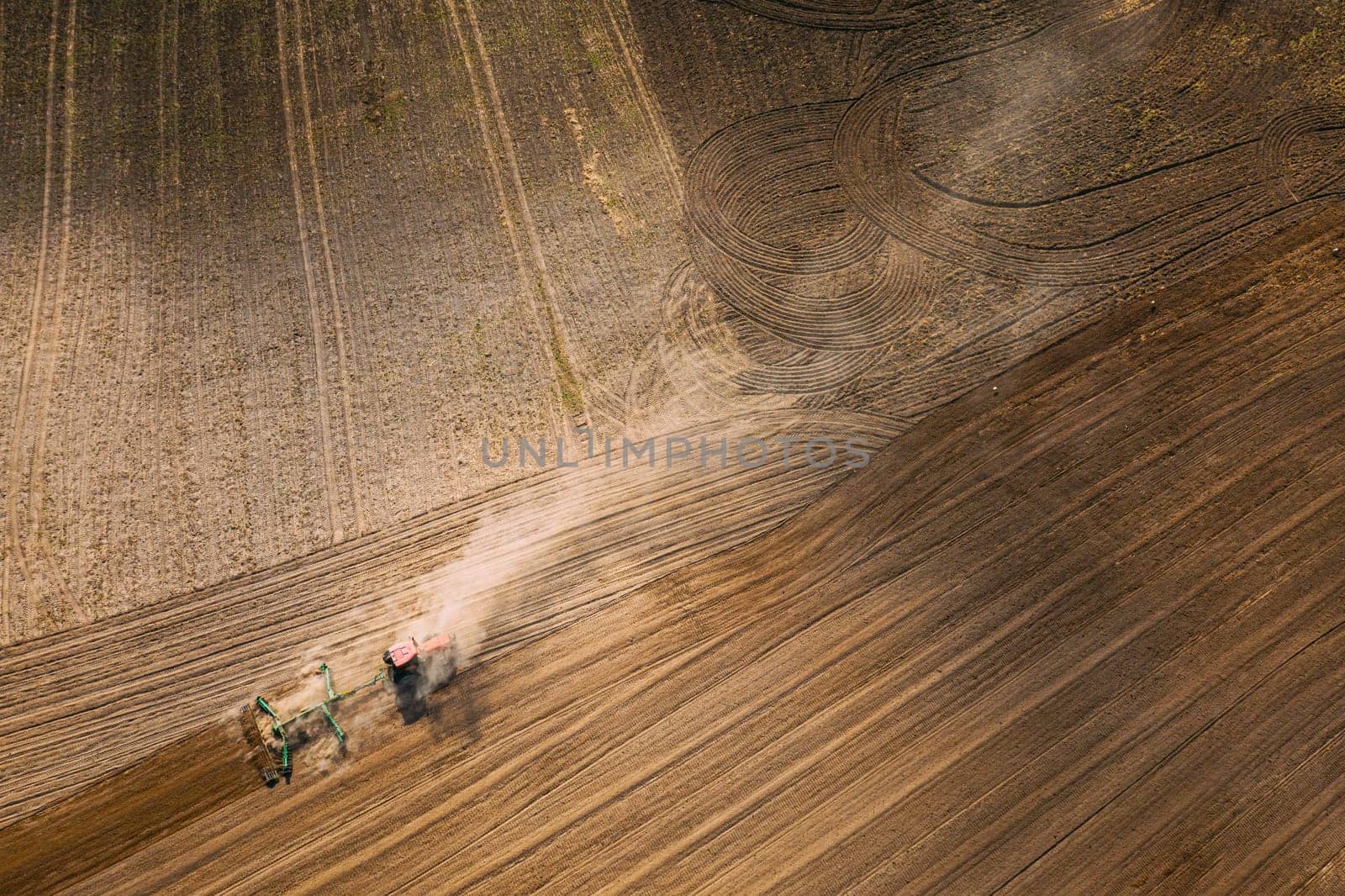Aerial View. Tractor Plowing Field. Beginning Of Agricultural Spring Season. Cultivator Pulled By A Tractor In Countryside Rural Field Landscape. Dust Rises From Under Plows.
