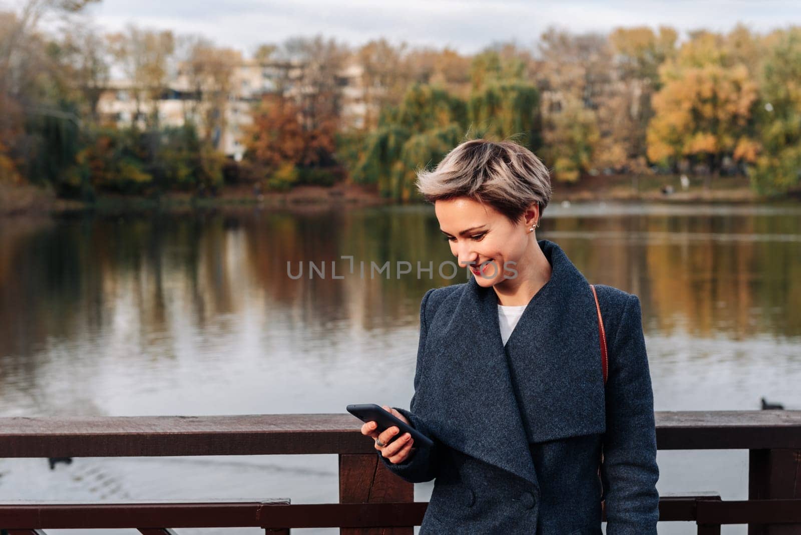 A woman in a city park by the river uses a smartphone.