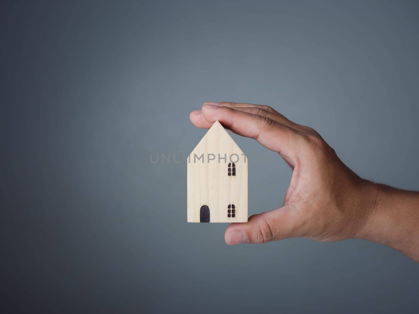Concept of selling a house. A hand is holding a model house on a gray background. Real estate agent offer house, property insurance and security, affordable housing concepts, home insurance broker agent, salesman person.