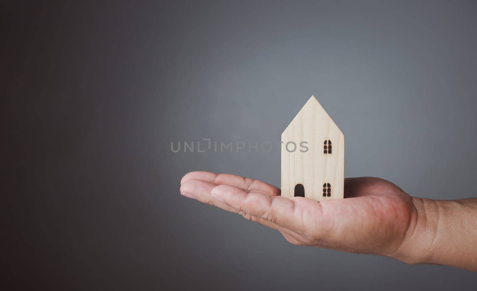 Concept of selling a house. A hand is holding a model house on a gray background. Real estate agent offer house, property insurance and security, affordable housing concepts, home insurance broker agent, salesman person.