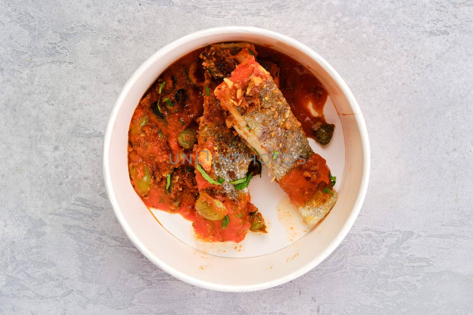 Top view of roasted zander served with steamed tomato, onion and olive sauce in take away cardboard package