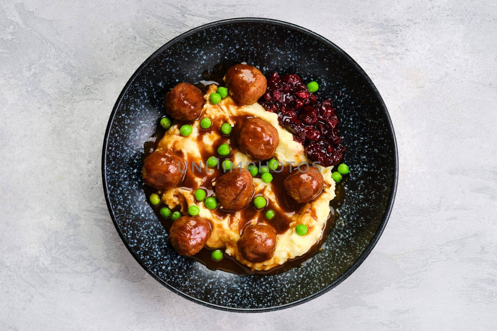 Top view of meatballs with gravy served with mashed potato, green pea and cranberry jam on a plate