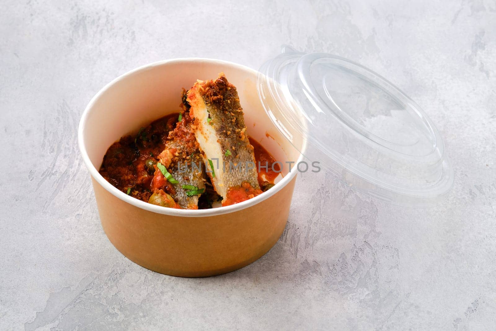 Roasted zander served with steamed tomato, onion and olive sauce in take away cardboard package