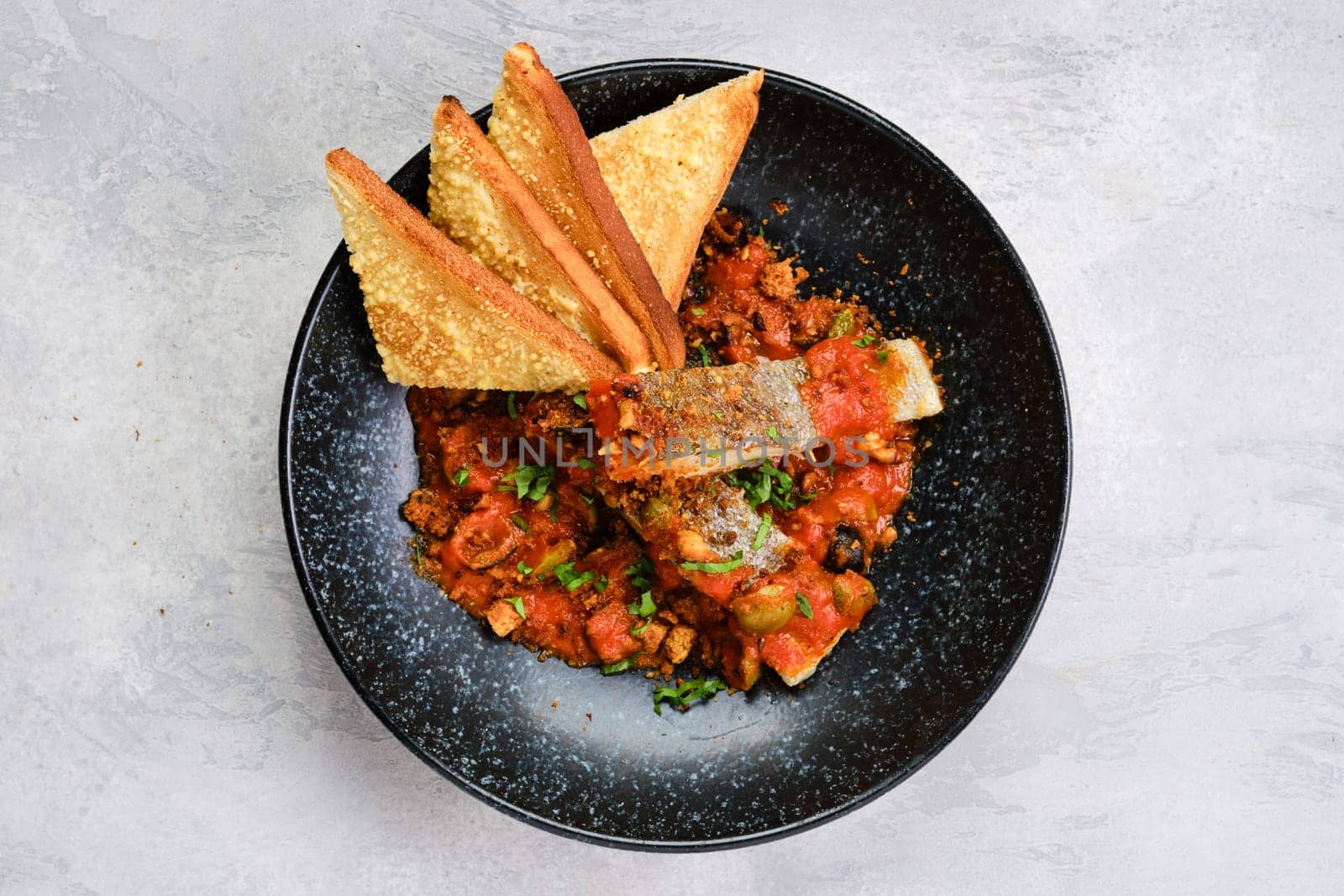 Top view of fried zander served with steamed tomato, onion and olive sauce  on a plate