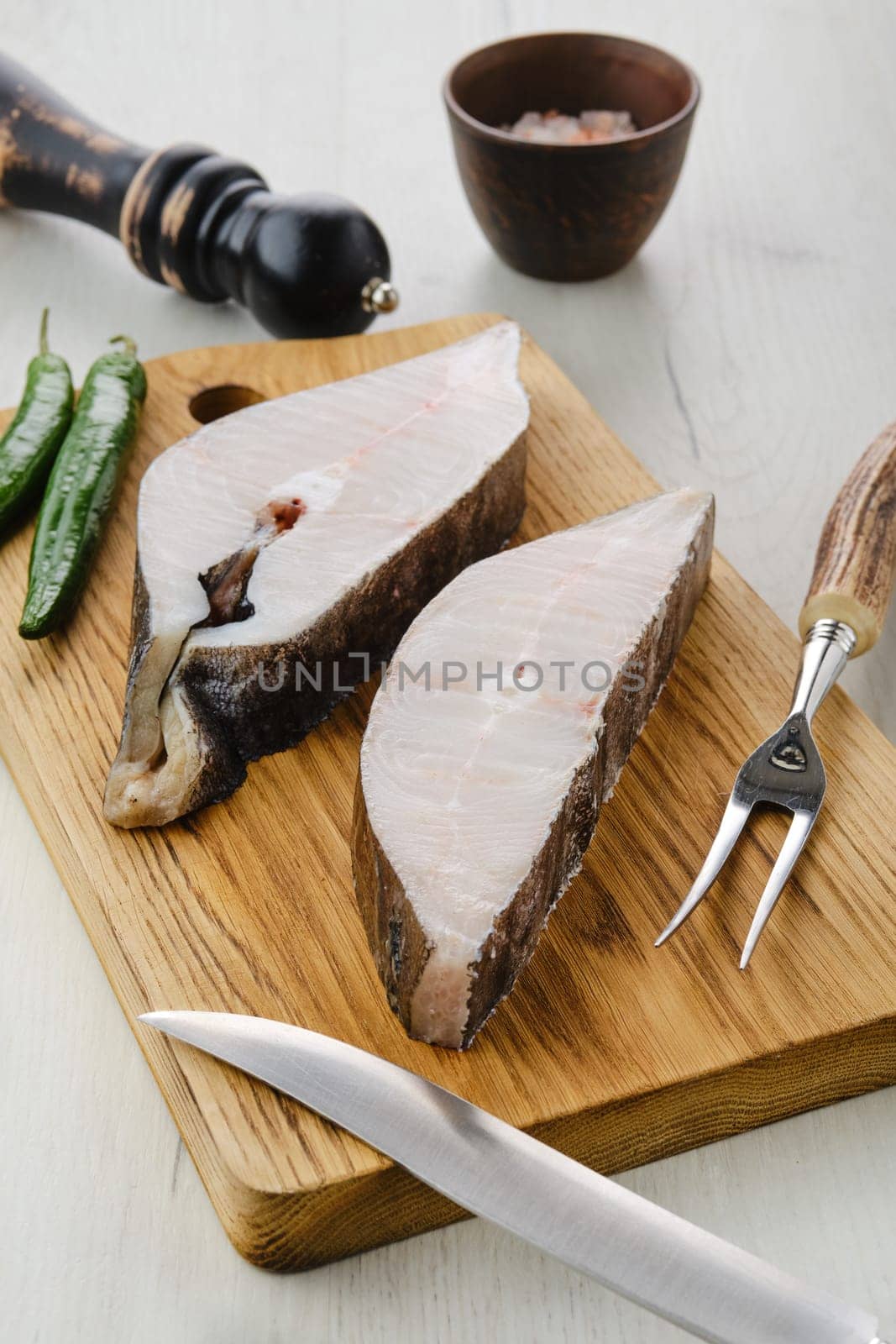 Closeup view of raw fresh halibut steak on wooden cutting board with spices