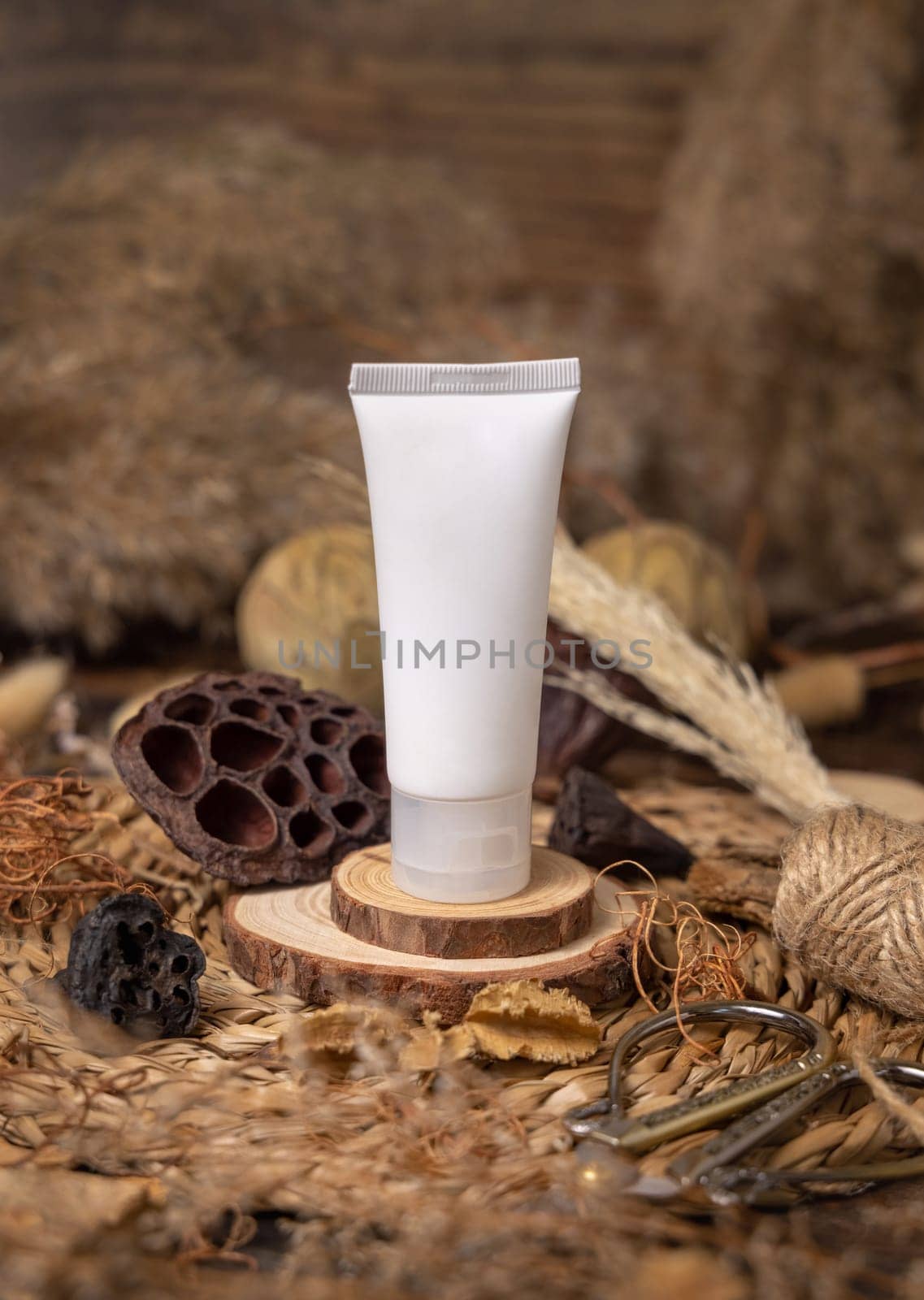 White plastic cosmetic tube on wood near natural decorations closeup, packaging mockup. Eco friendly skincare product, lotion or cream. Bohemian composition with dried leaves and flowers.