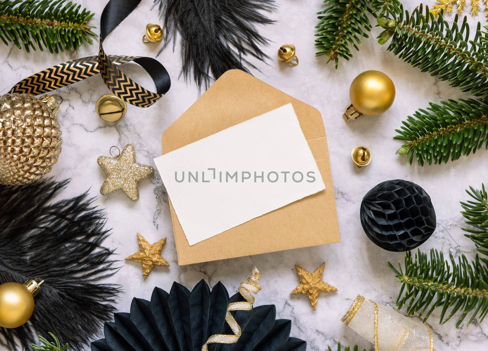 Paper card and envelope between black and golden Christmas decorations and fir tree branches top view. Winter flat lay with blank invitation card, Mockup, copy space