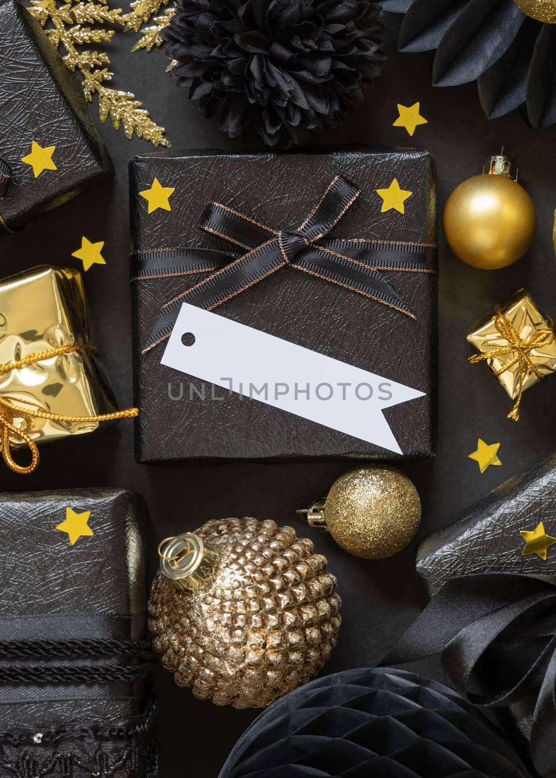 Black and golden Christmas Gift Boxes with a bow and ornaments close up, horizontal paper gift tag mockup, copy space. Dark winter composition with blank label card for Christmas, New Year, Birthday, Anniversary
