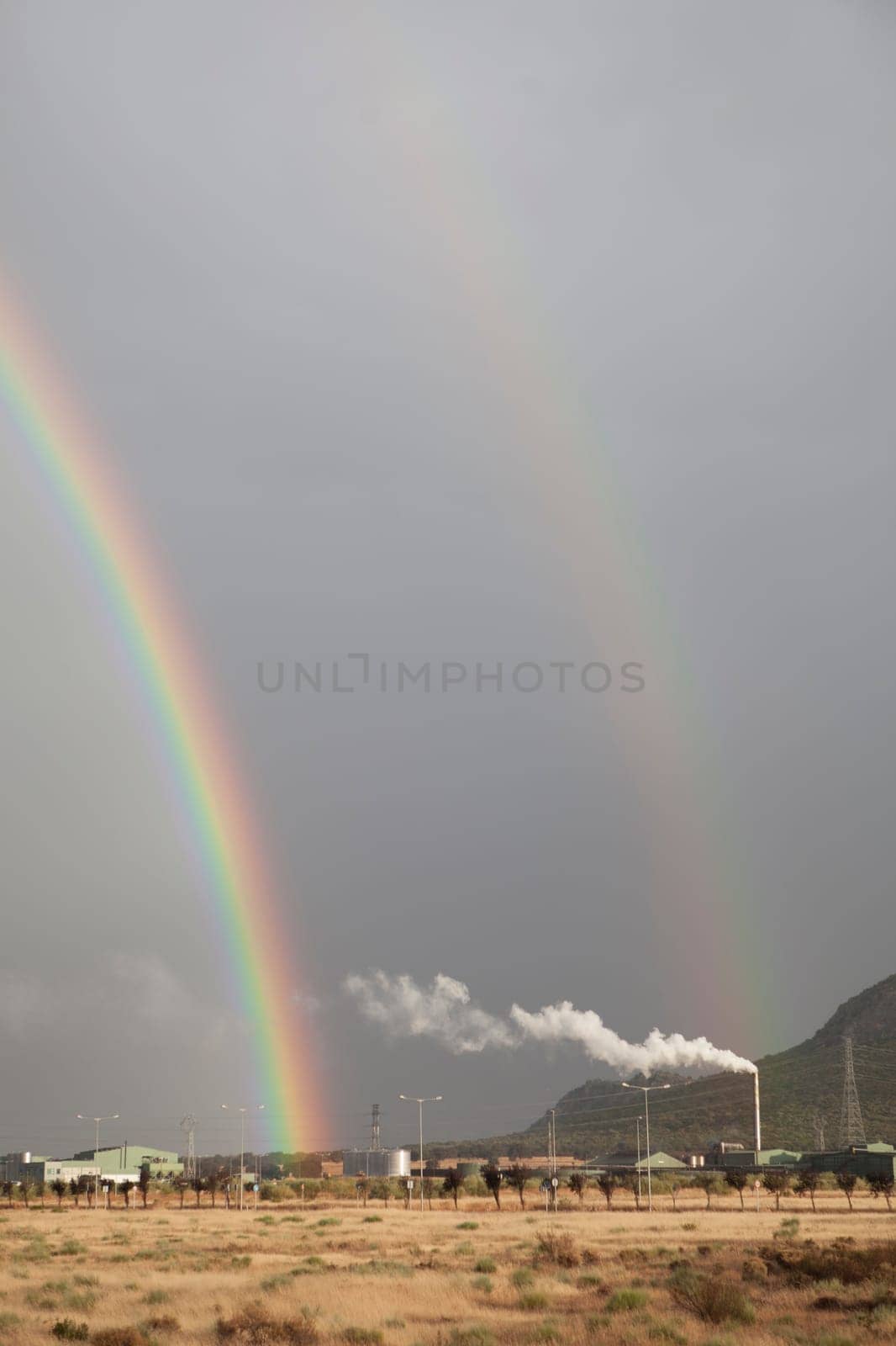 Double rainbow rising over an industrial area. Primary and secondary rainbows are visible