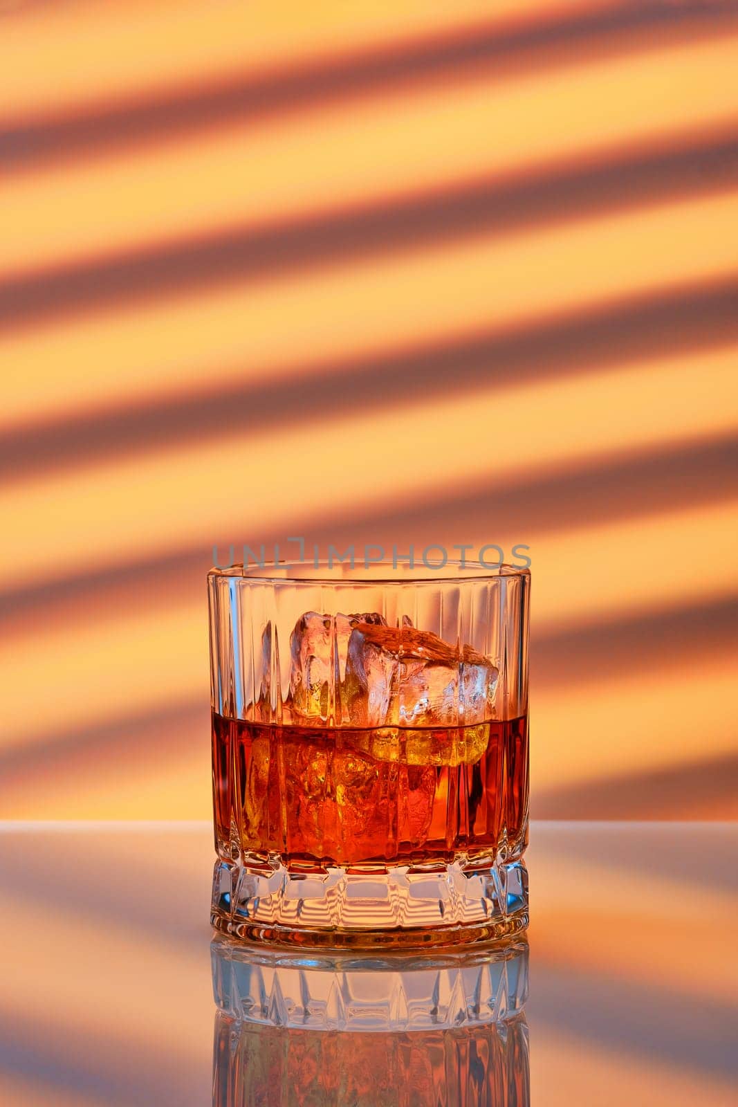 Whiskey with ice in facetted rocks glass over striped background