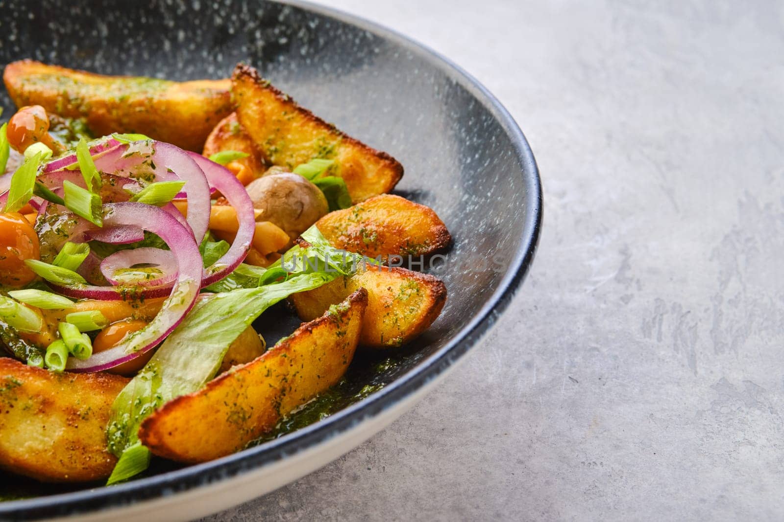 Closeup view of fried potato wedges with champignons dressed with red and white onion