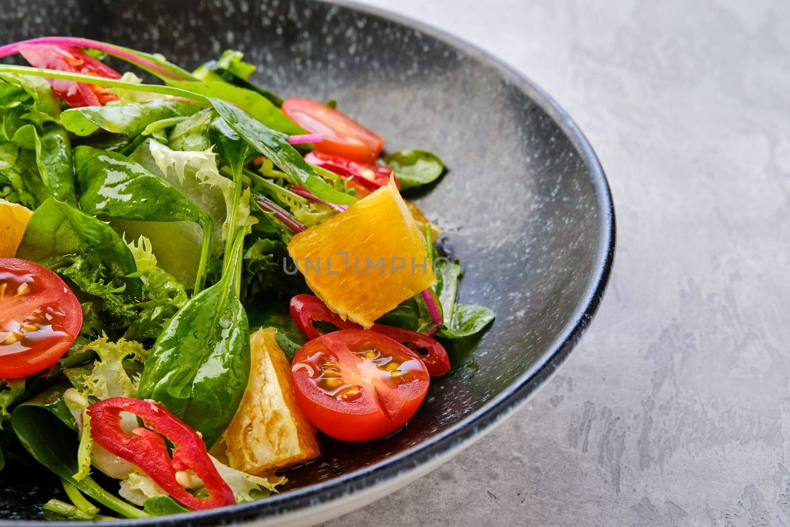 Closeup view of spicy salad with orange, chilli pepper, tomato, cucumber and avocado