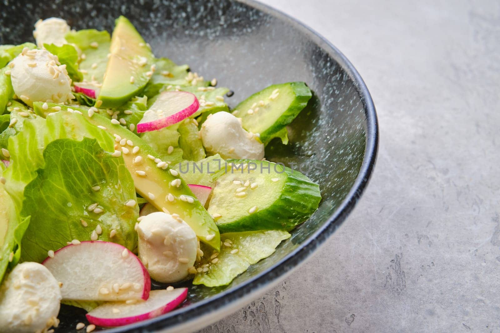 Closeup view of salad with lettuce, avocado, radish and mozzarella dressed with sesame