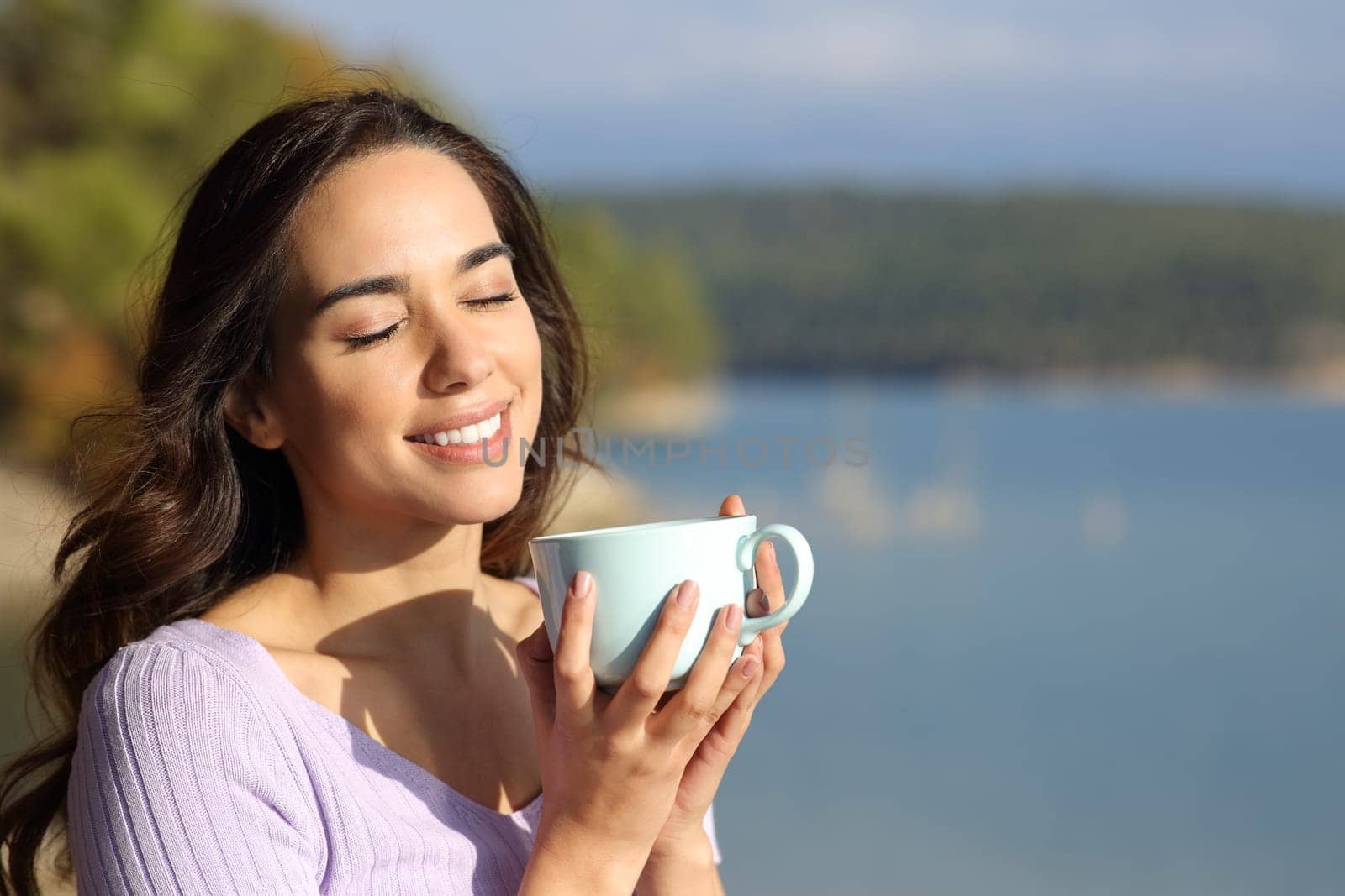 Happy woman enjoying holding coffee mug a sunny day in nature