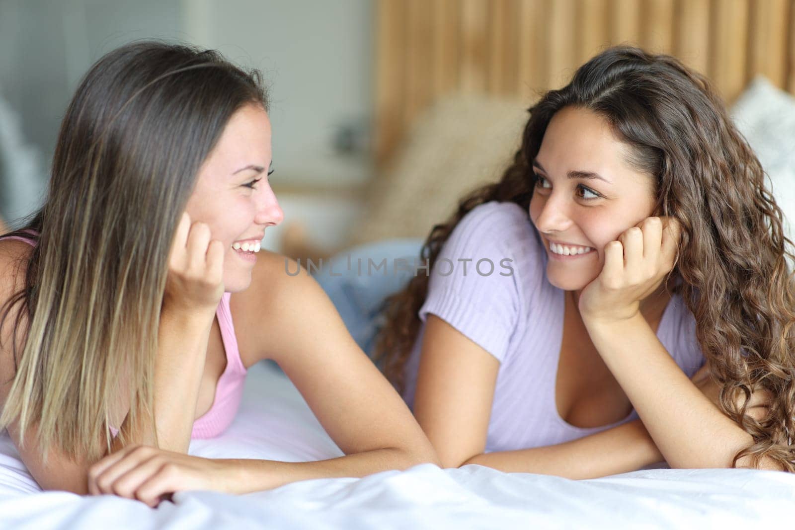 Two happy women looking each other lying on a bed in the bedroom