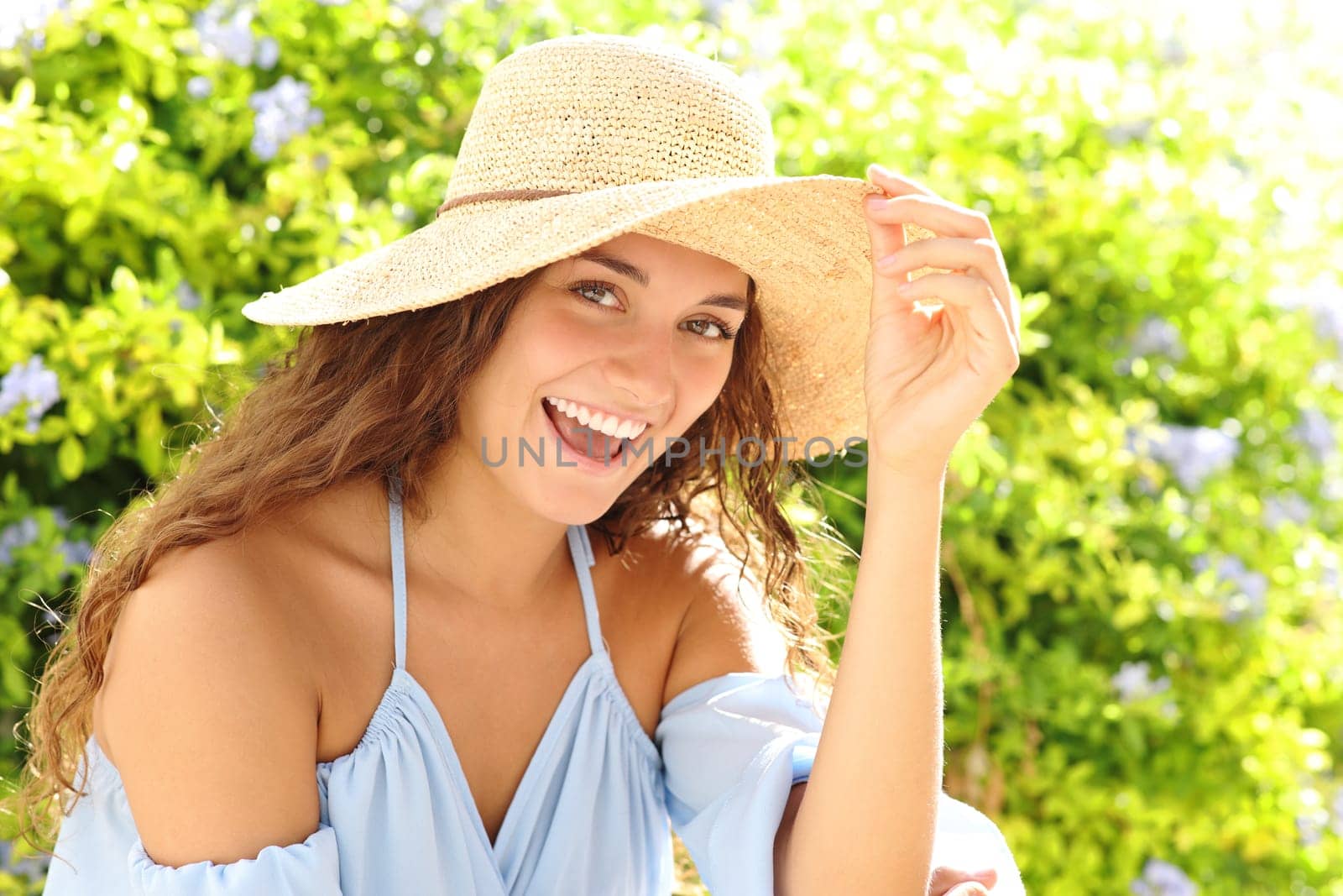 Happy woman with pamela hat looks at you in a green garden