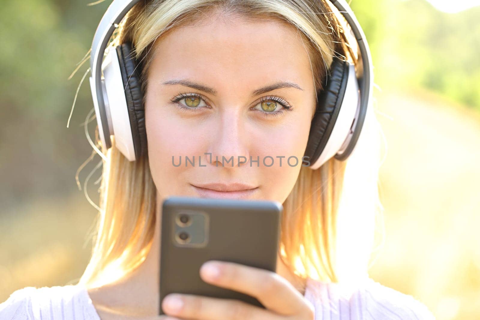 Front view portrait of a woman wearing wireless headphones holding smart phone looking at you