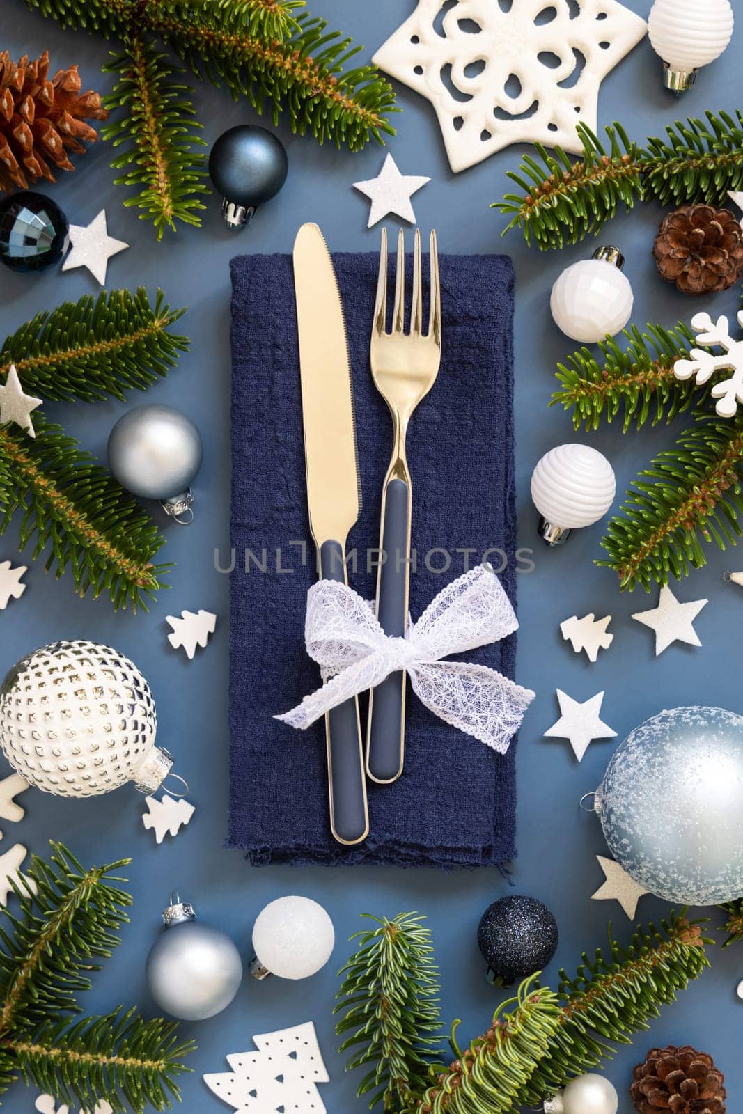 Blue and white Christmas table setting with decorations and fir tree branches top view. Winter table with fork, knife and plate. Winter New Year or Christmas dinner atmosphere
