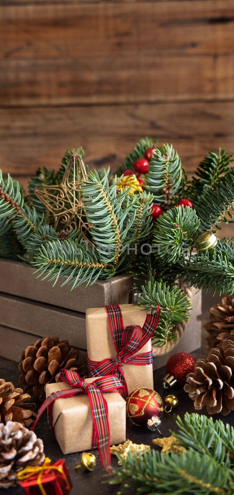 Wrapped gift boxes between Christmas decorations, pine cones and green fir branches close up on wooden background, copy space. Christmas or New Year Holiday atmosphere flat lay