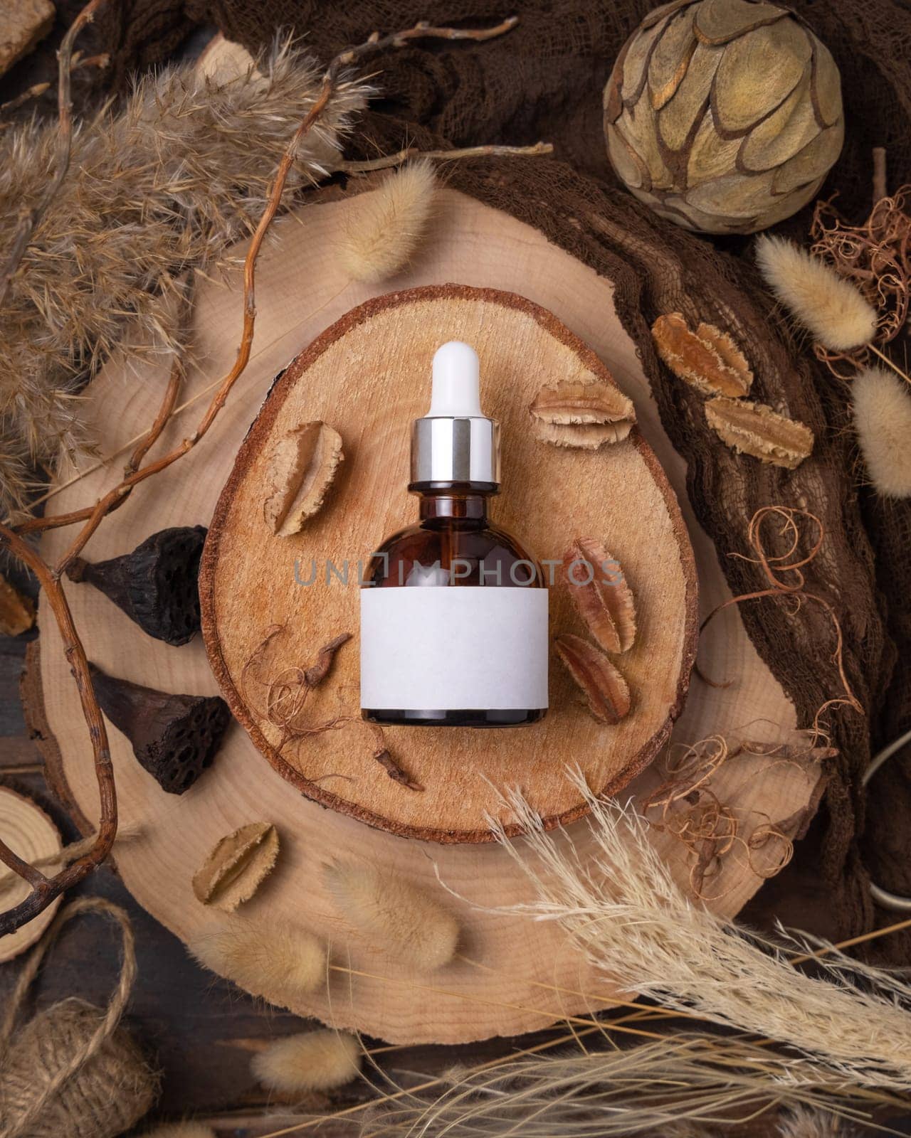 Glass dropper bottle on wood near natural boho decorations top view, label mockup. Skincare beauty product, serum or essence. Bohemian eco friendly cosmetics flat lay with dried leaves.
